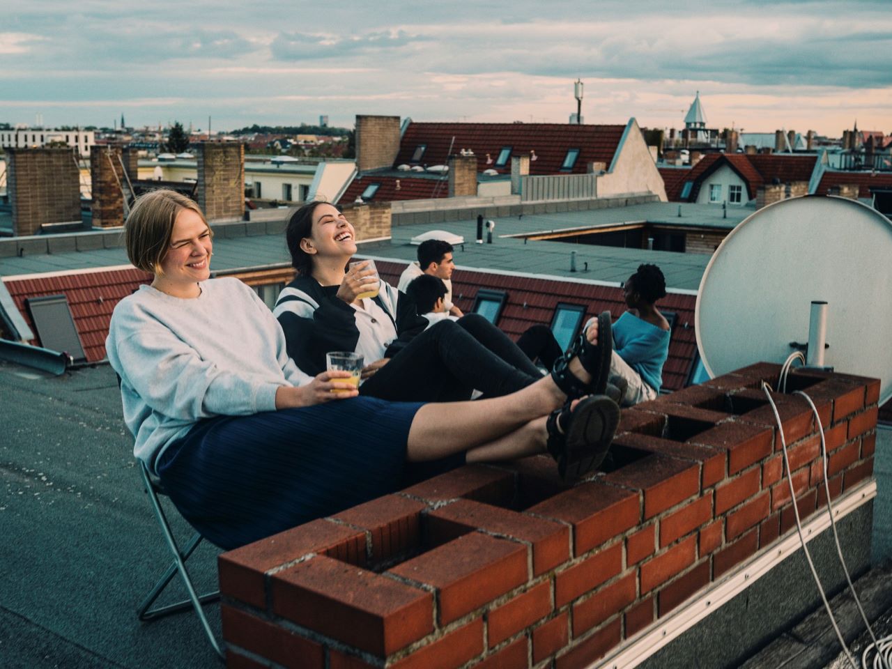 Mehrere Jugendliche sitzen mit Getränken auf einem Hausdach und freuen sich
